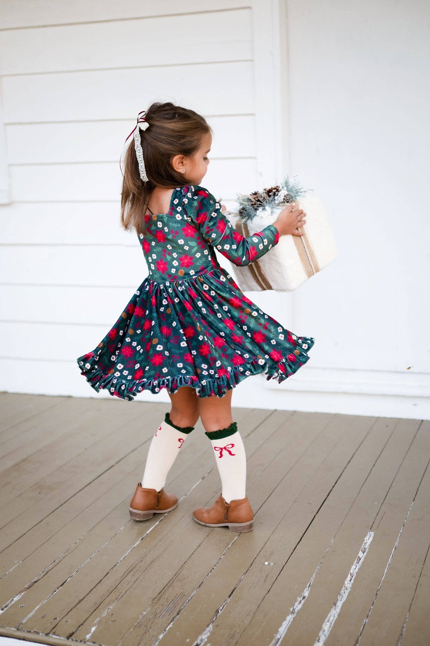 Young girl in a floral dress standing on a wooden deck.