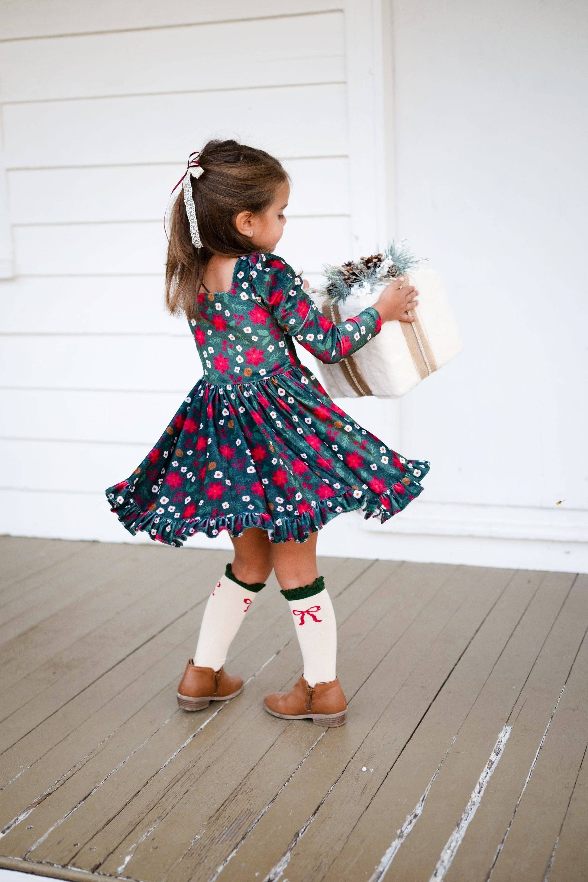 Young girl in a floral dress standing on a wooden deck.