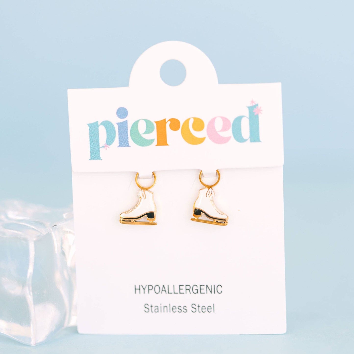 Gold ice skate earrings on a 'pierceed' branded card with a light blue background