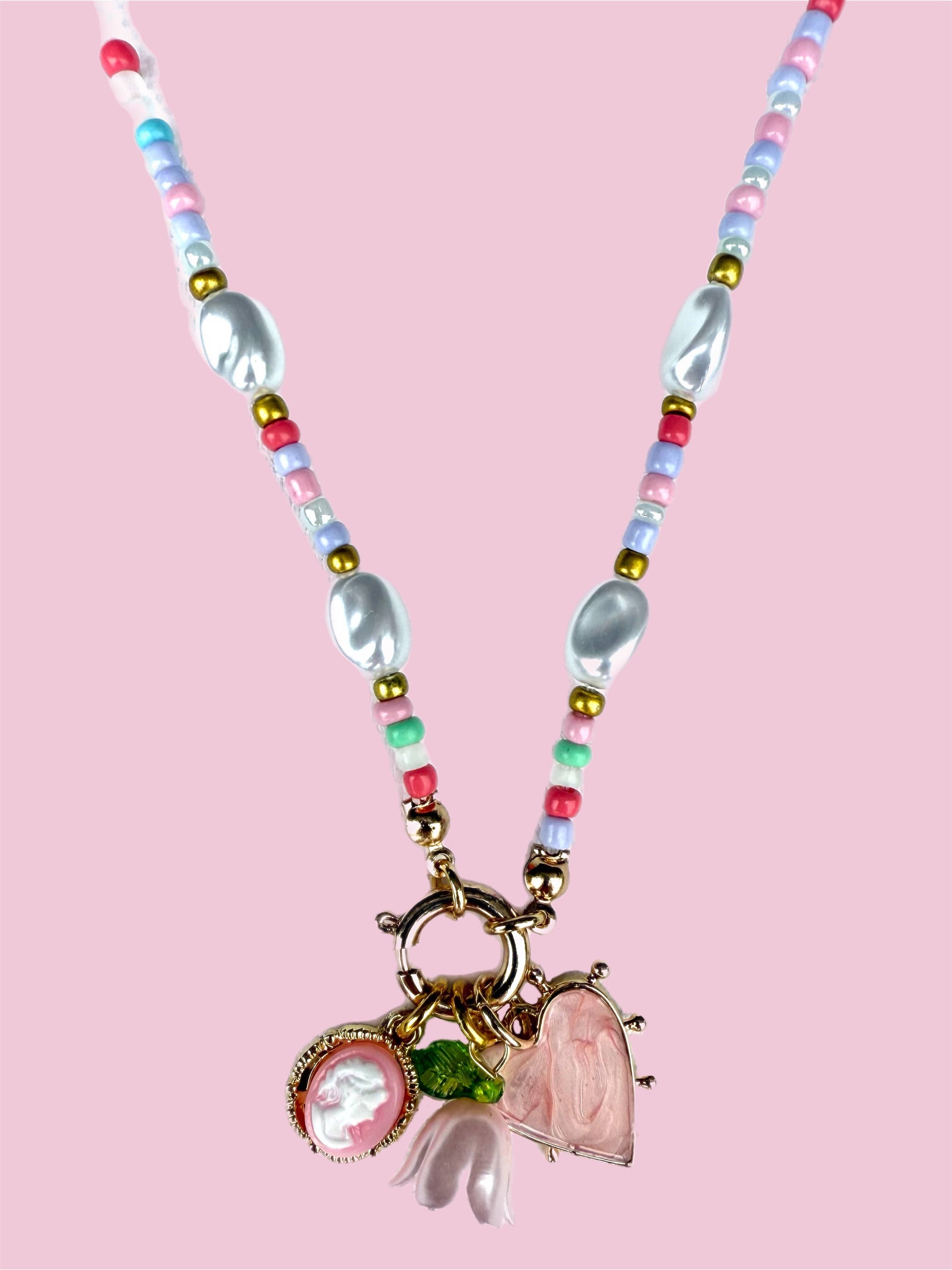 Necklace with colorful beads and heart-shaped pendants on a pink background
