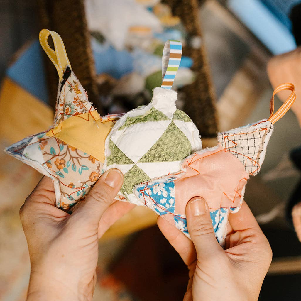 Hands holding small fabric bags with colorful patterns against a blurred indoor background