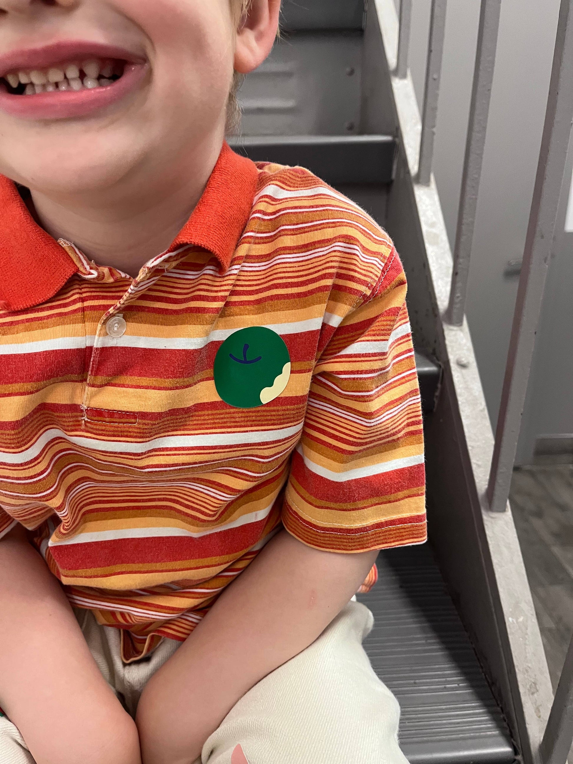 Child wearing a colorful striped polo shirt with a green patch sitting on a chair.