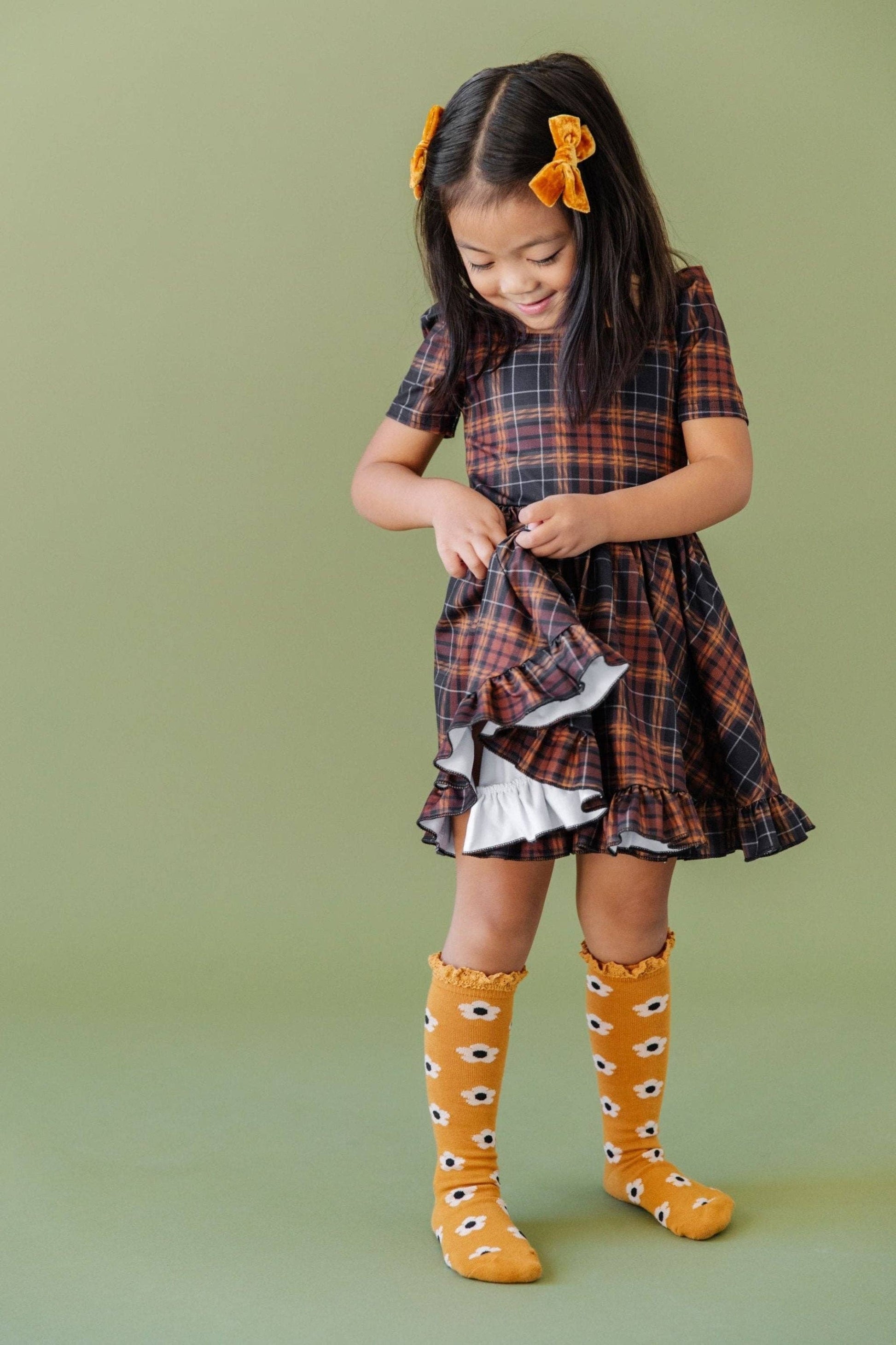 Young girl wearing a plaid dress and mustard-colored socks with black dots on a green background