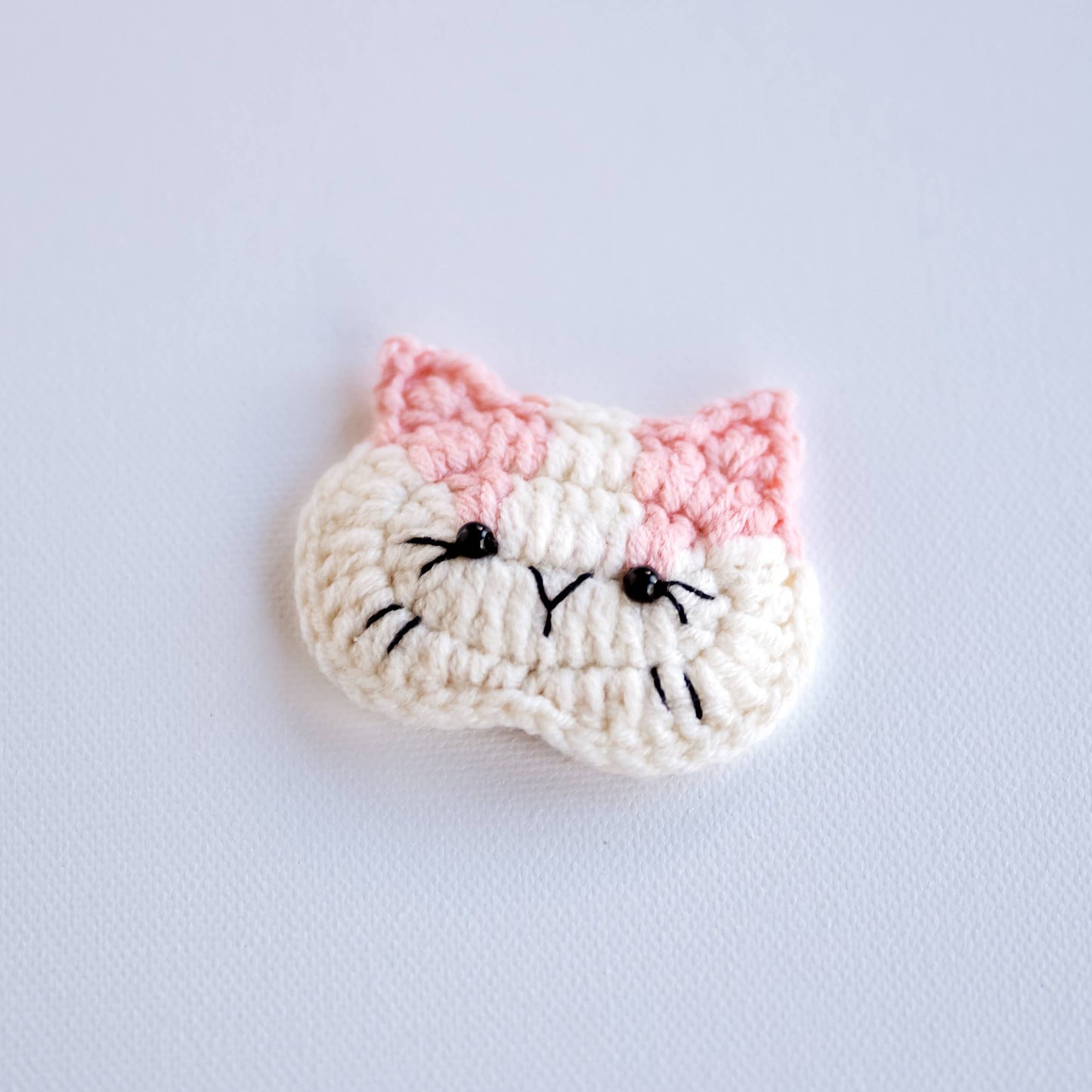 Crocheted cat face pattern on a light gray background