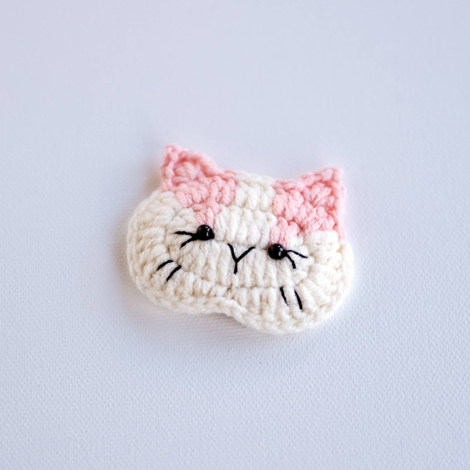 Crocheted cat face pattern on a light gray background