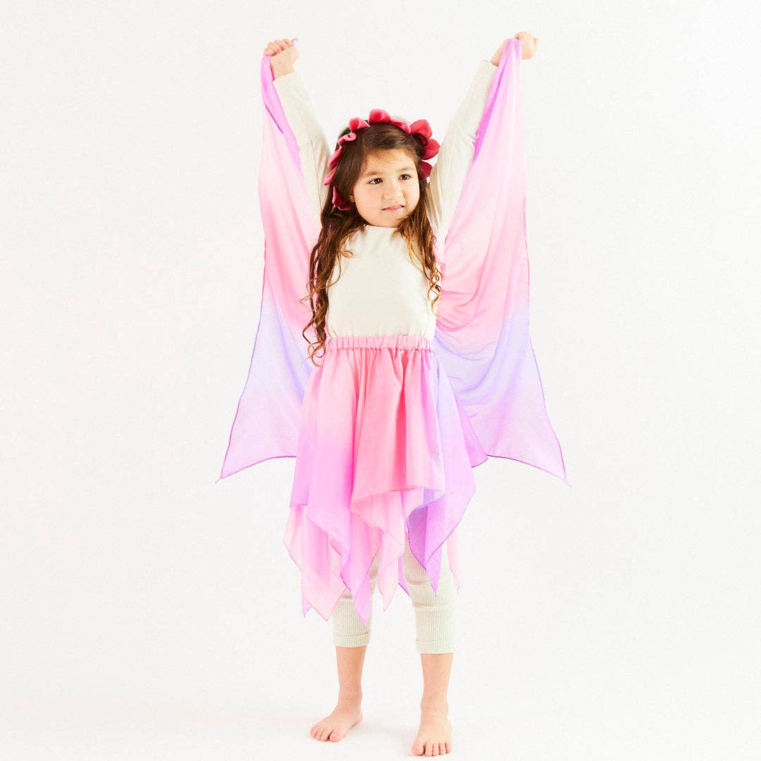 Young girl wearing a pink and purple cape on a white background
