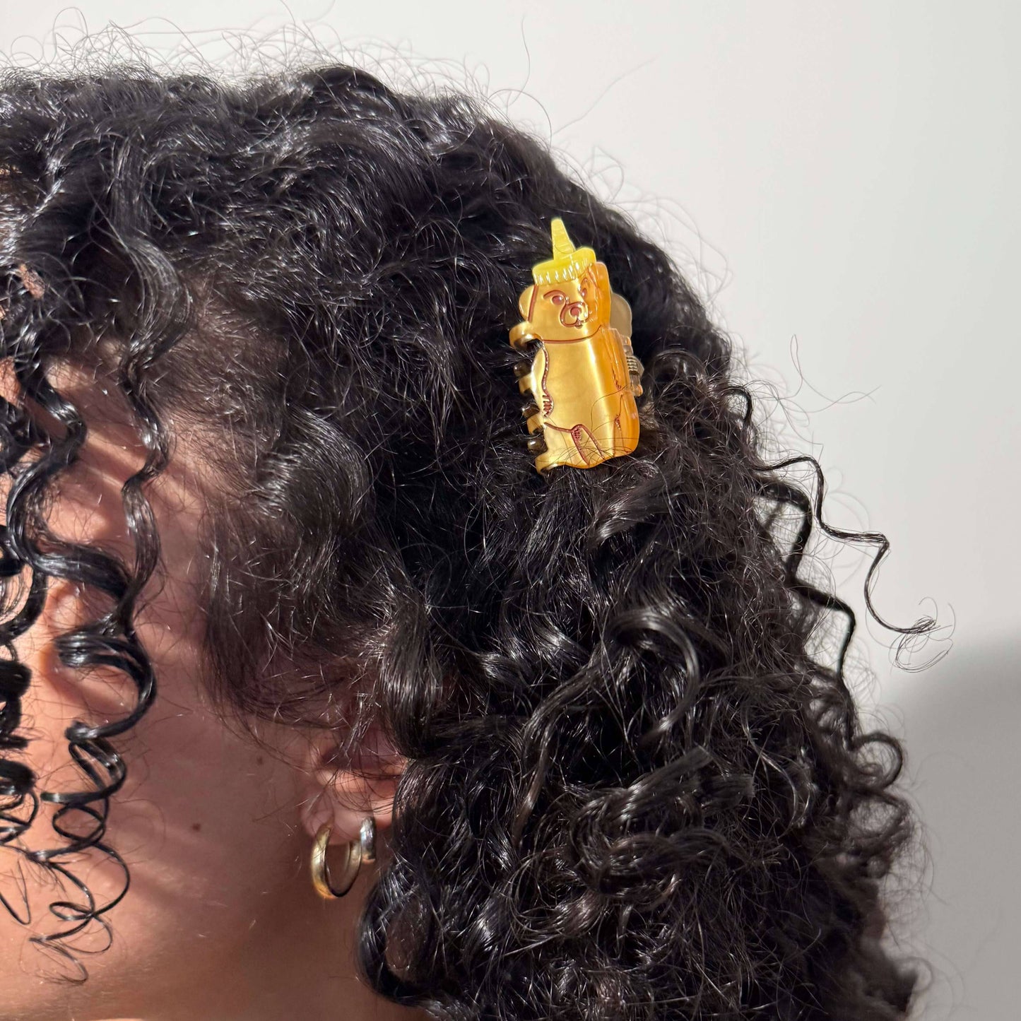 Close-up of a person's hair with a gold hair clip featuring a face design.
