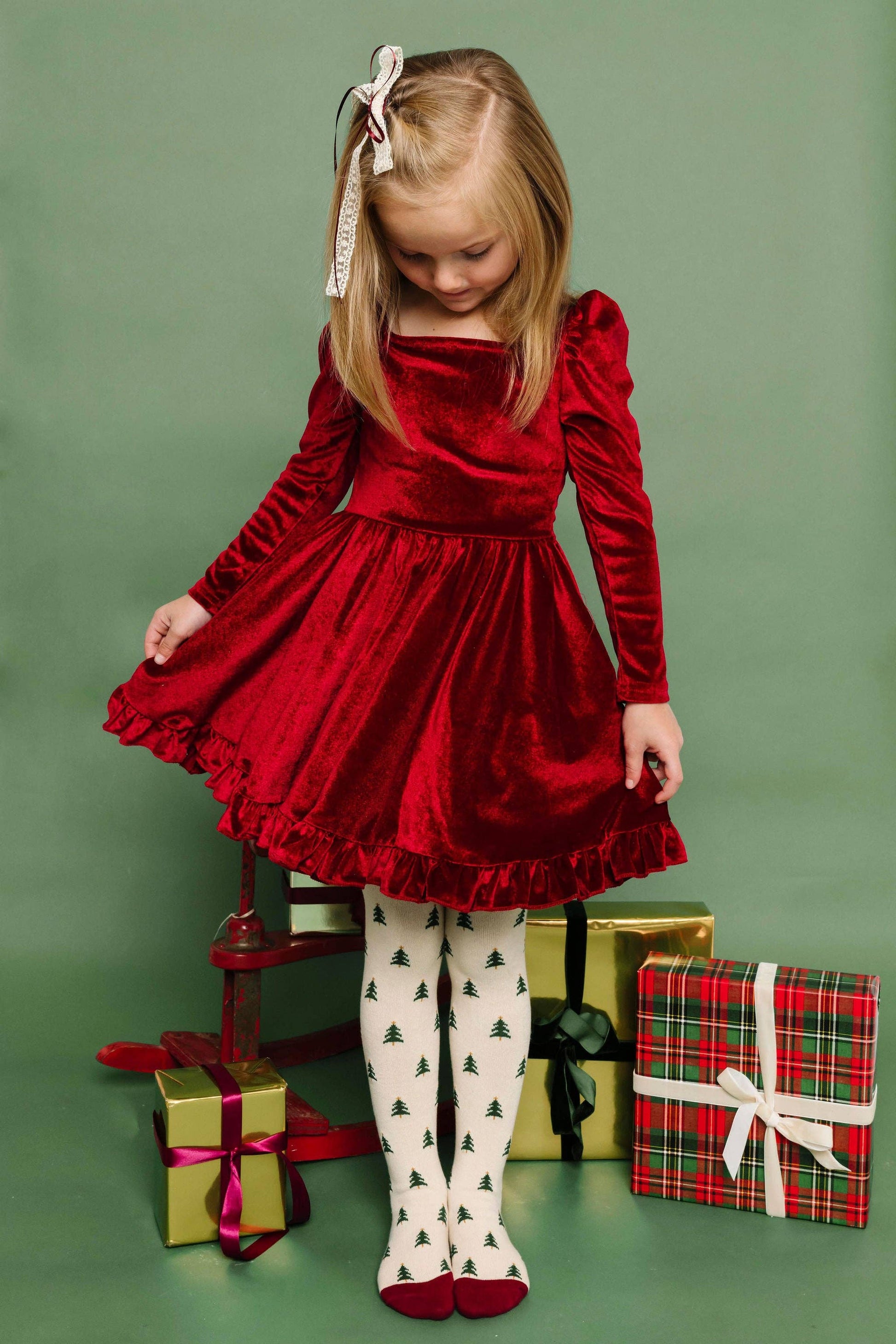 Young girl in a red velvet dress with Christmas presents on a green background