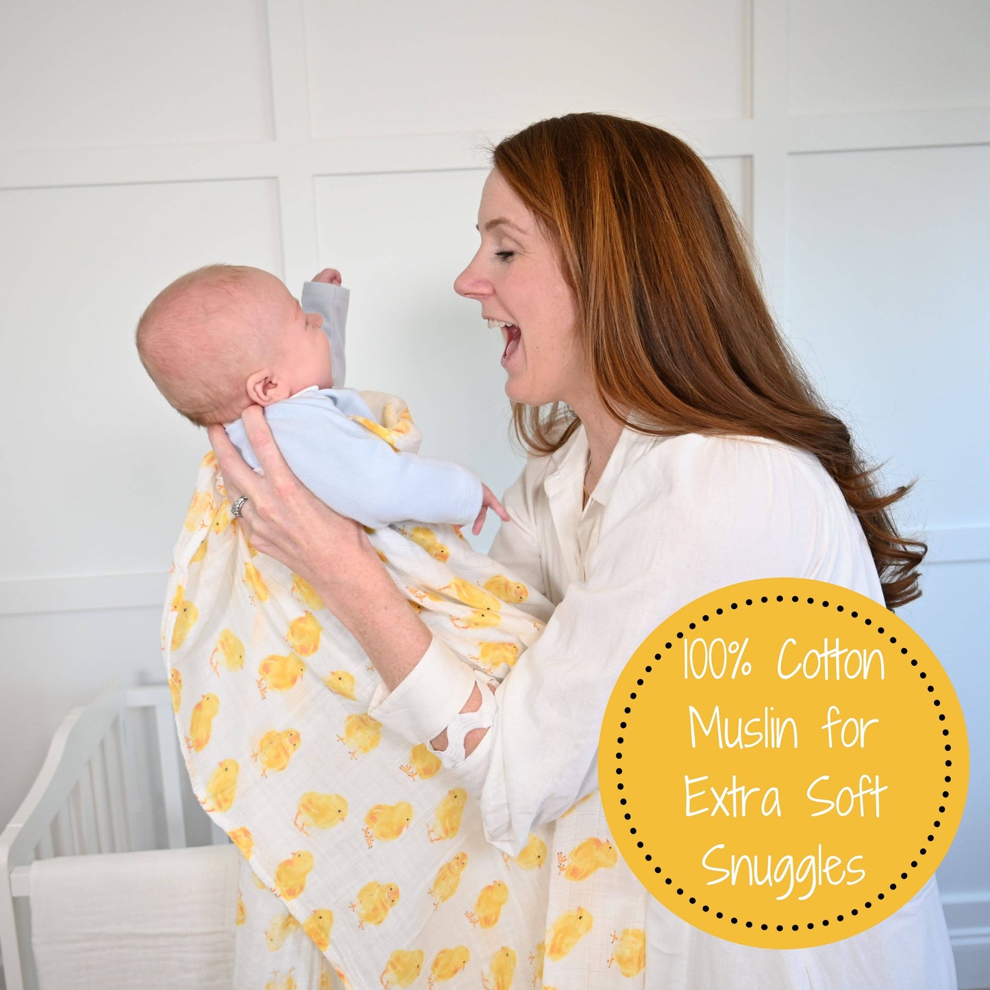 Woman holding a baby wrapped in a yellow and white patterned blanket with text about 100% cotton muslin.