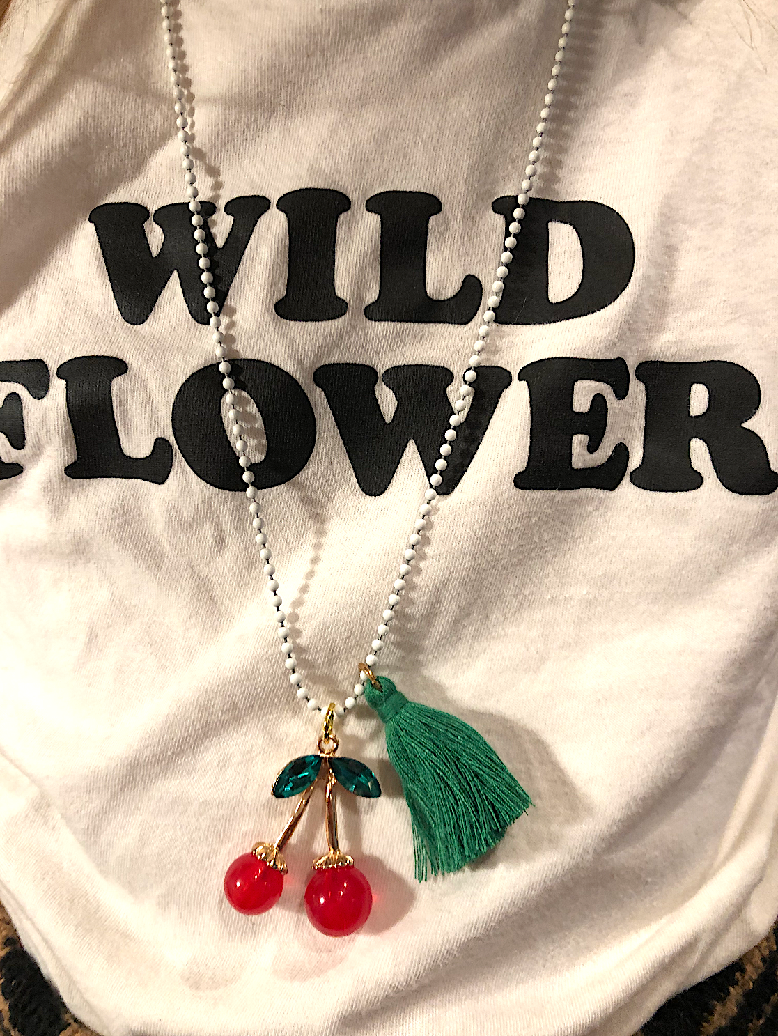 Necklace with cherry and tassel pendant on a shirt with 'Wild Flower' text