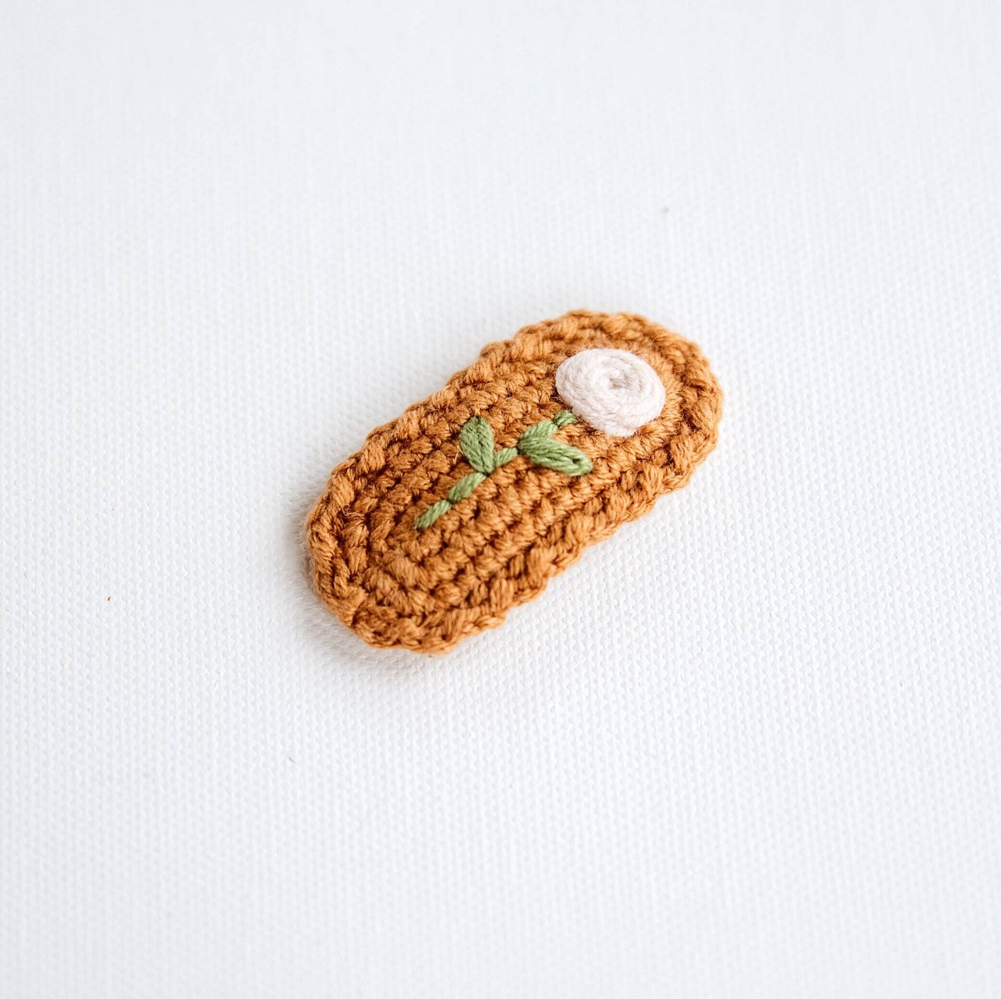 Crocheted hair clip with a white top and green leaves on a light background
