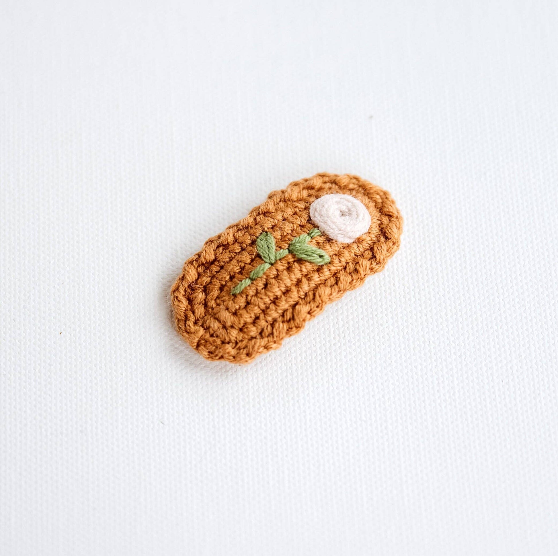 Crocheted hair clip with a white top and green leaves on a light background