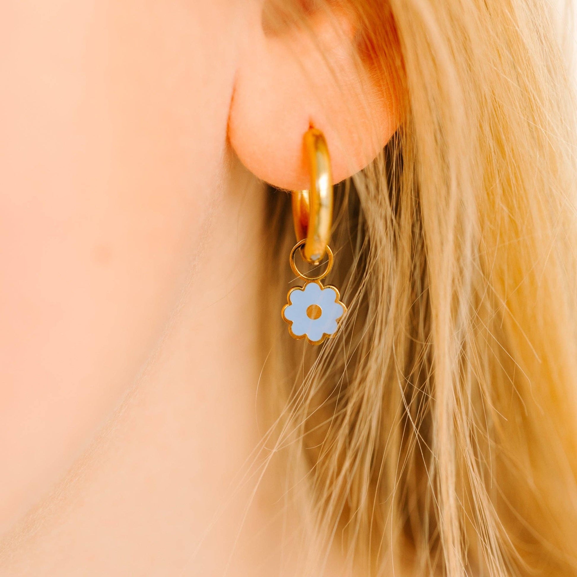 Gold hoop earring with a blue flower charm worn by a person with blonde hair.