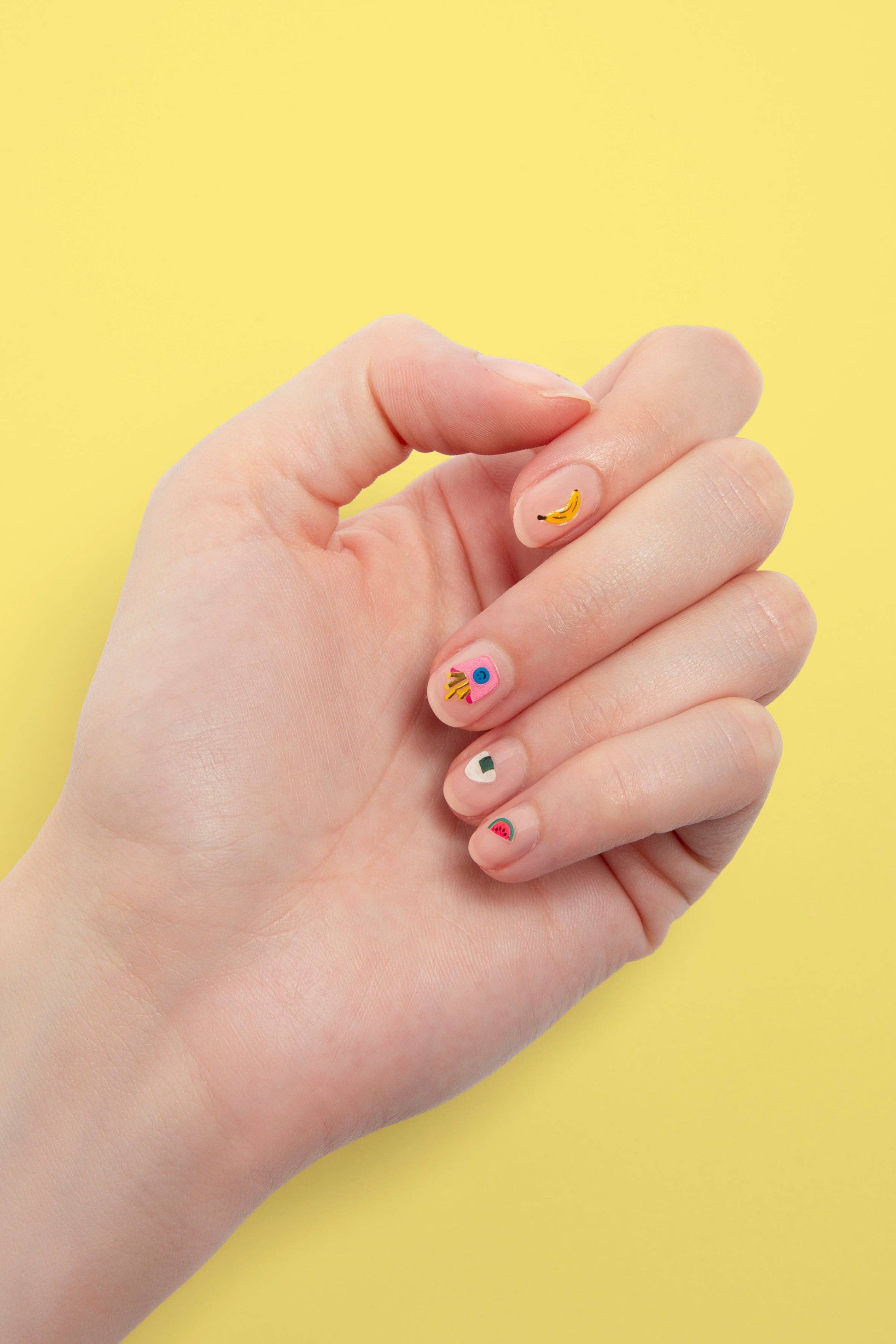 Close-up of a hand with decorated nails against a yellow background