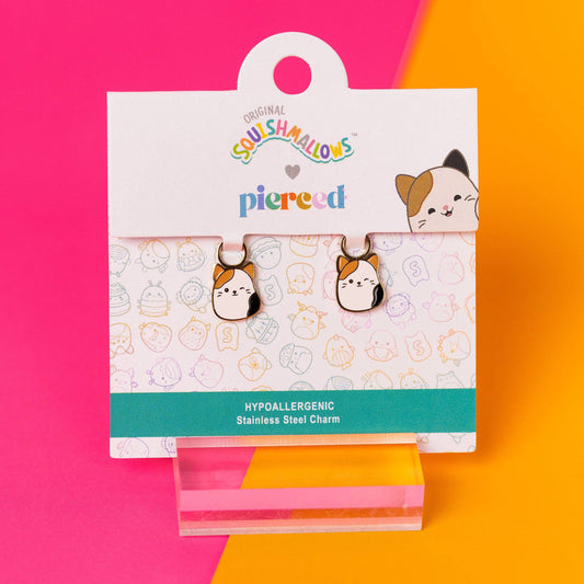 Pair of cat-shaped earrings in a 'piecred' branded packaging on a pink and orange background.