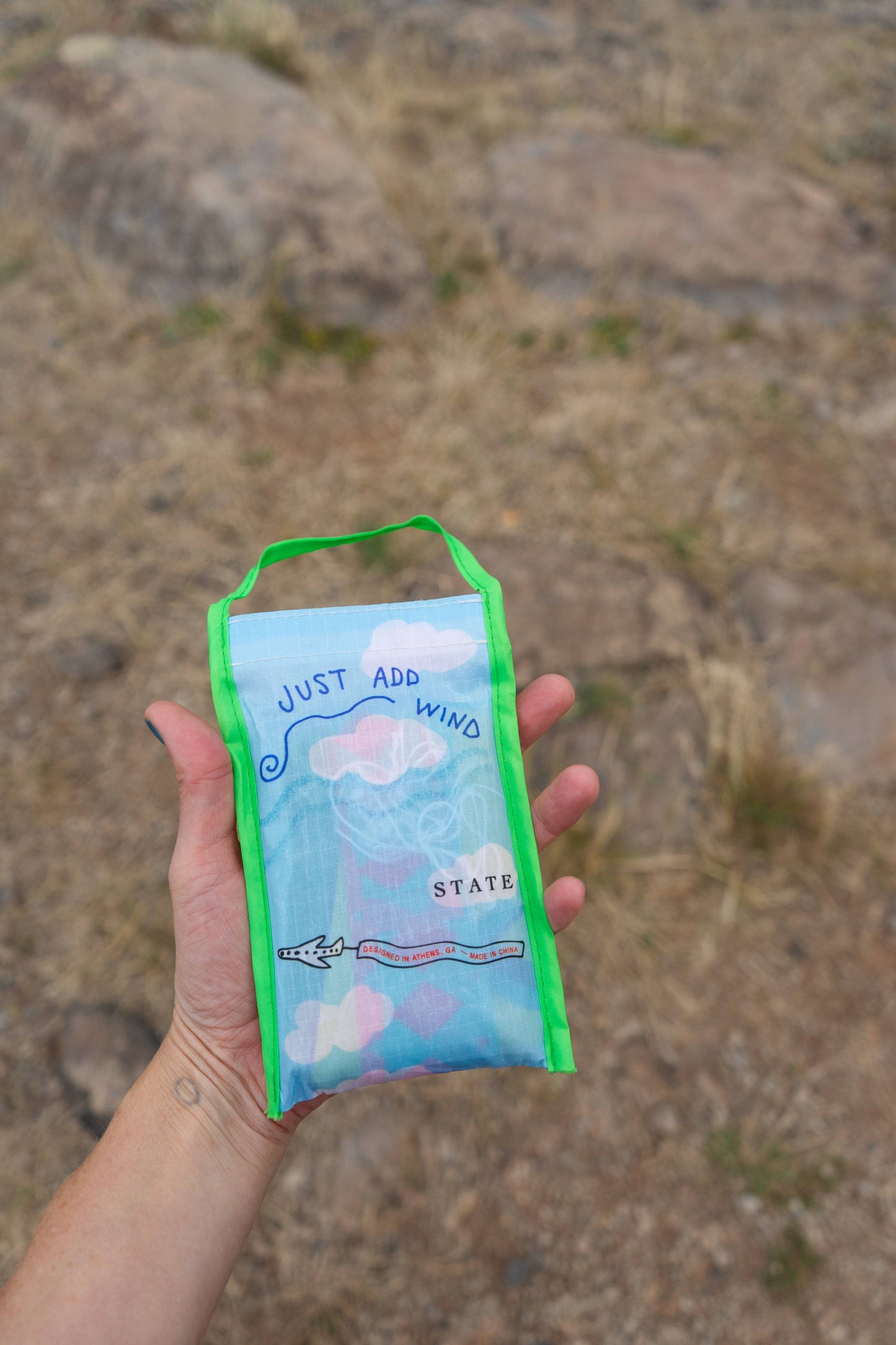 Hand holding a small blue pouch with green strap against a rocky background