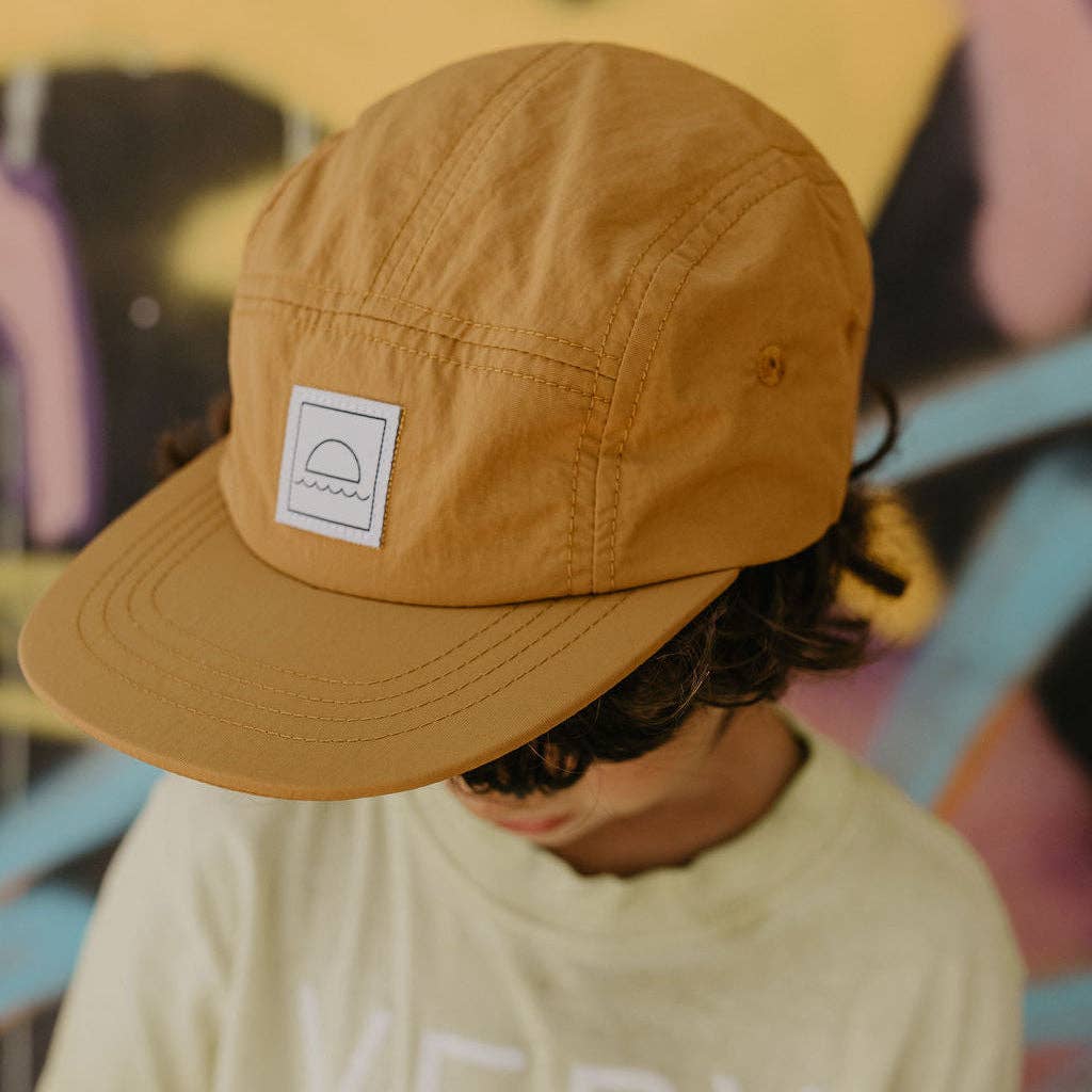 Person wearing a brown cap with a logo, blurred background