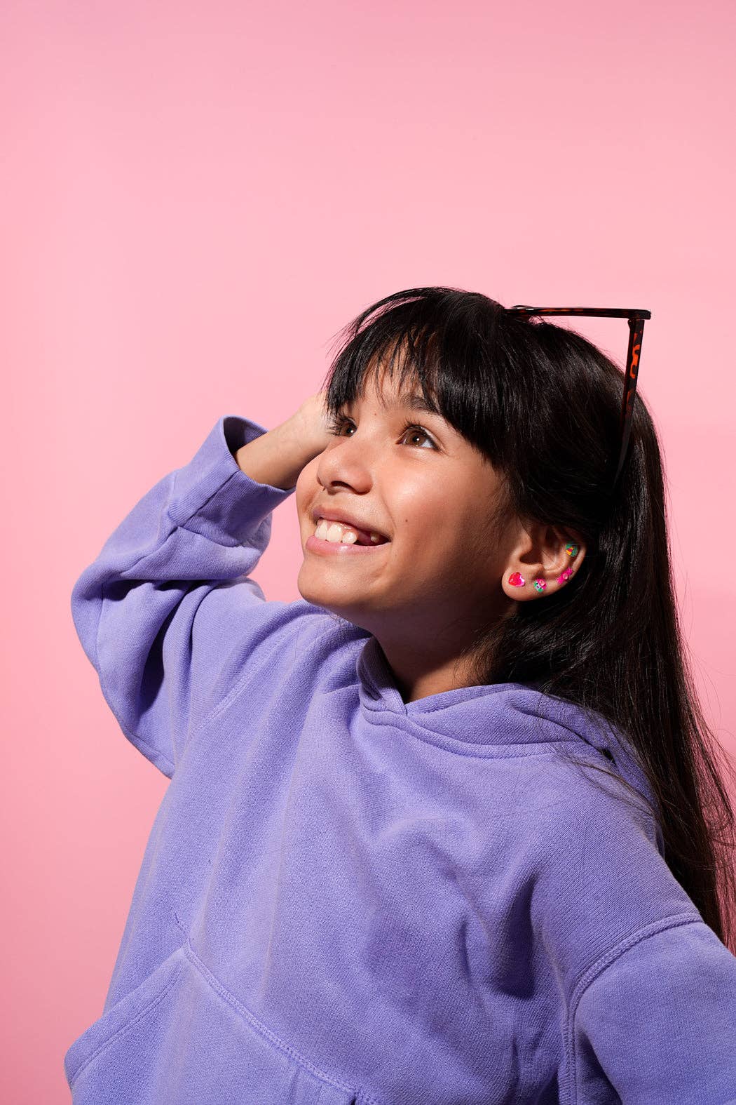 Young girl wearing a purple hoodie against a pink background