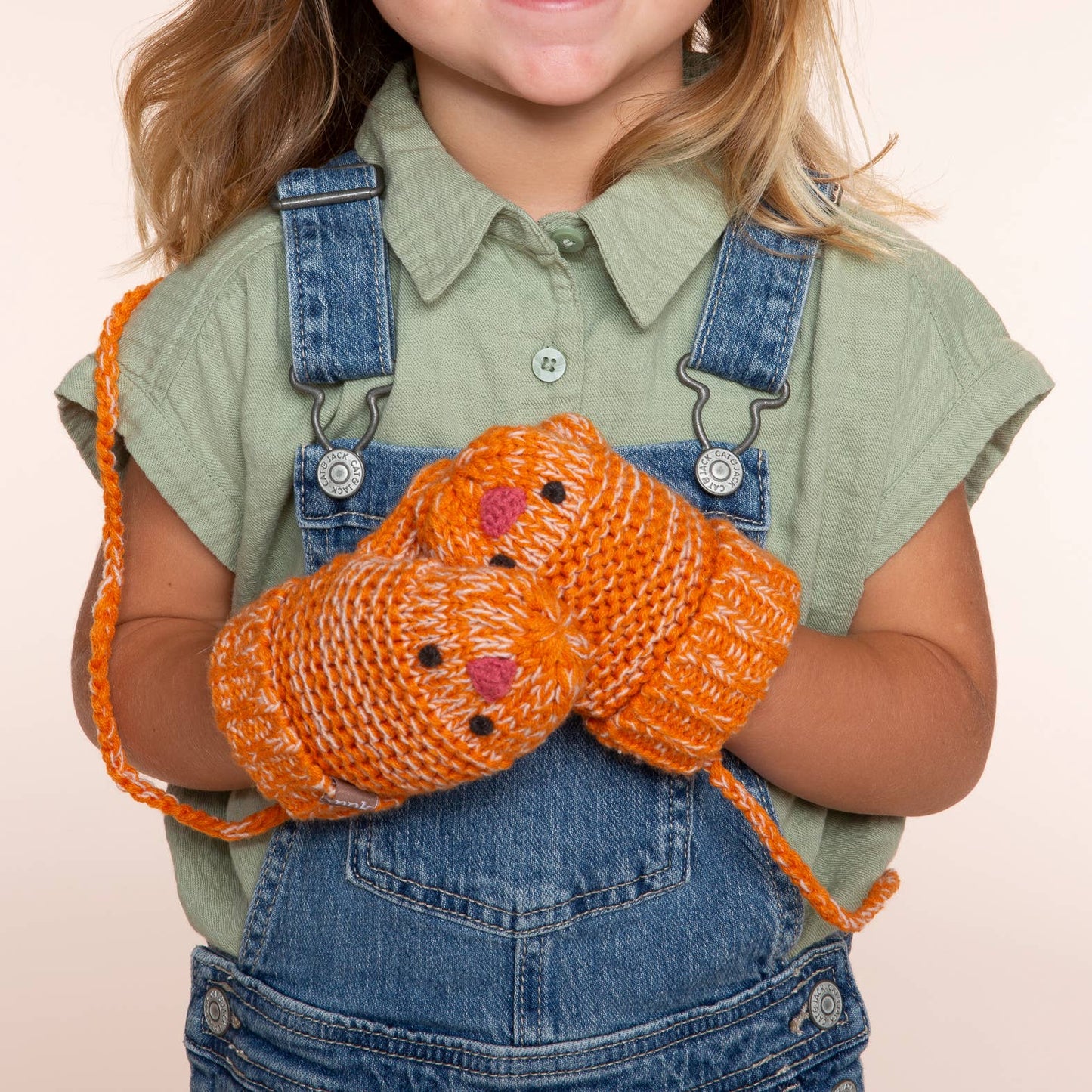 Child wearing orange knitted gloves on a beige background