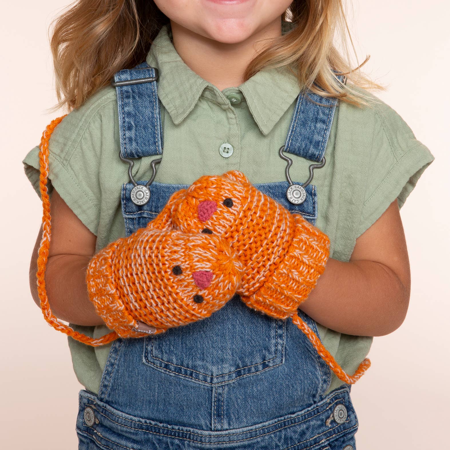 Child wearing orange knitted gloves on a beige background
