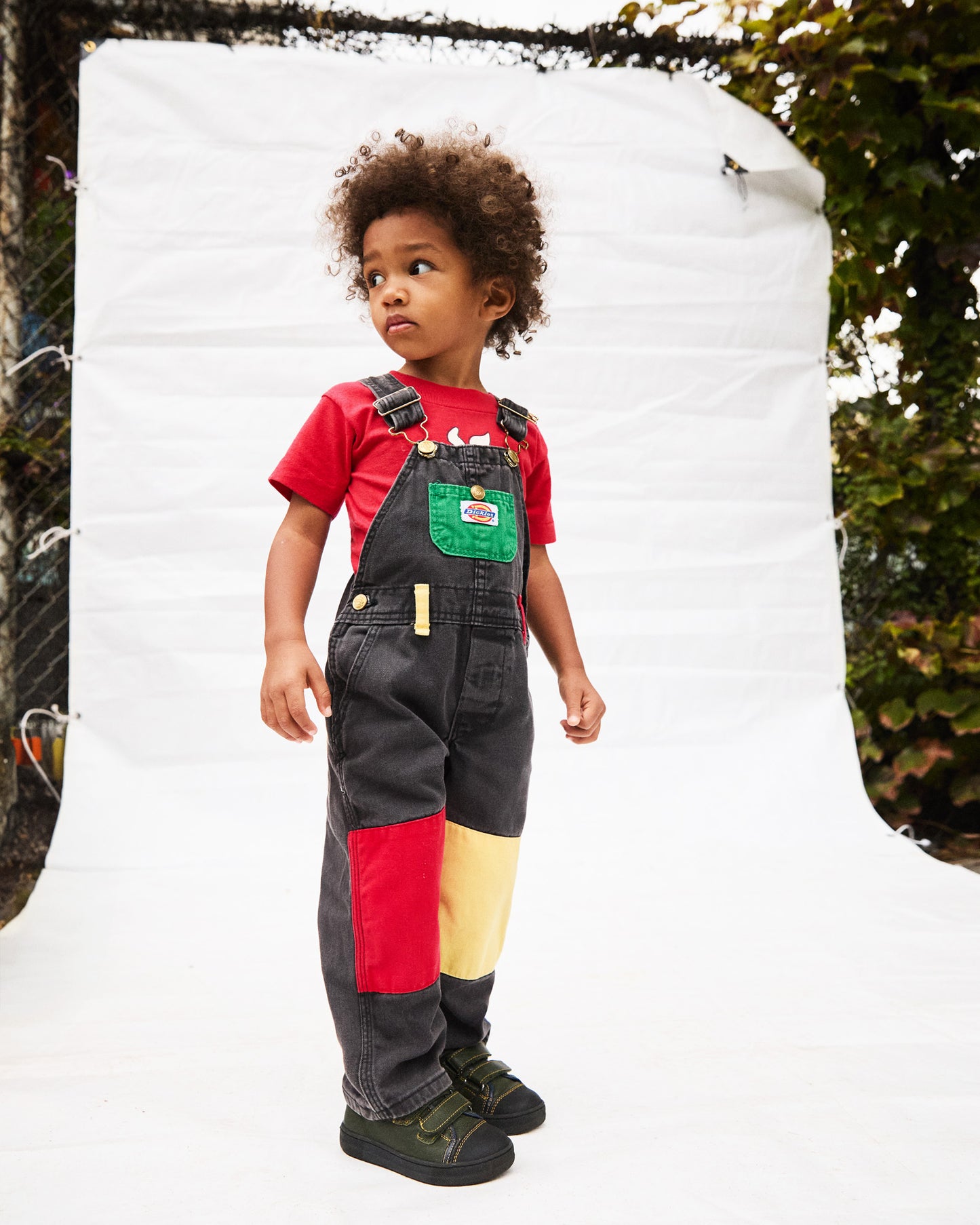 Child wearing colorful overalls and a red shirt with a white background