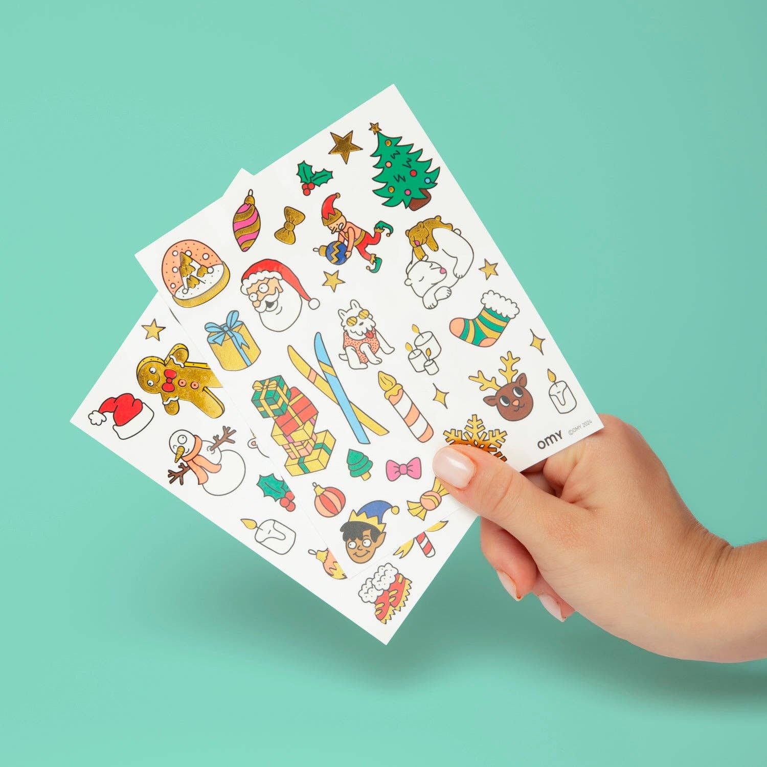 Hand holding a sheet of Christmas-themed stickers against a teal background