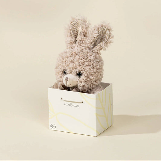 Plush toy with bunny ears in a white box on a beige background