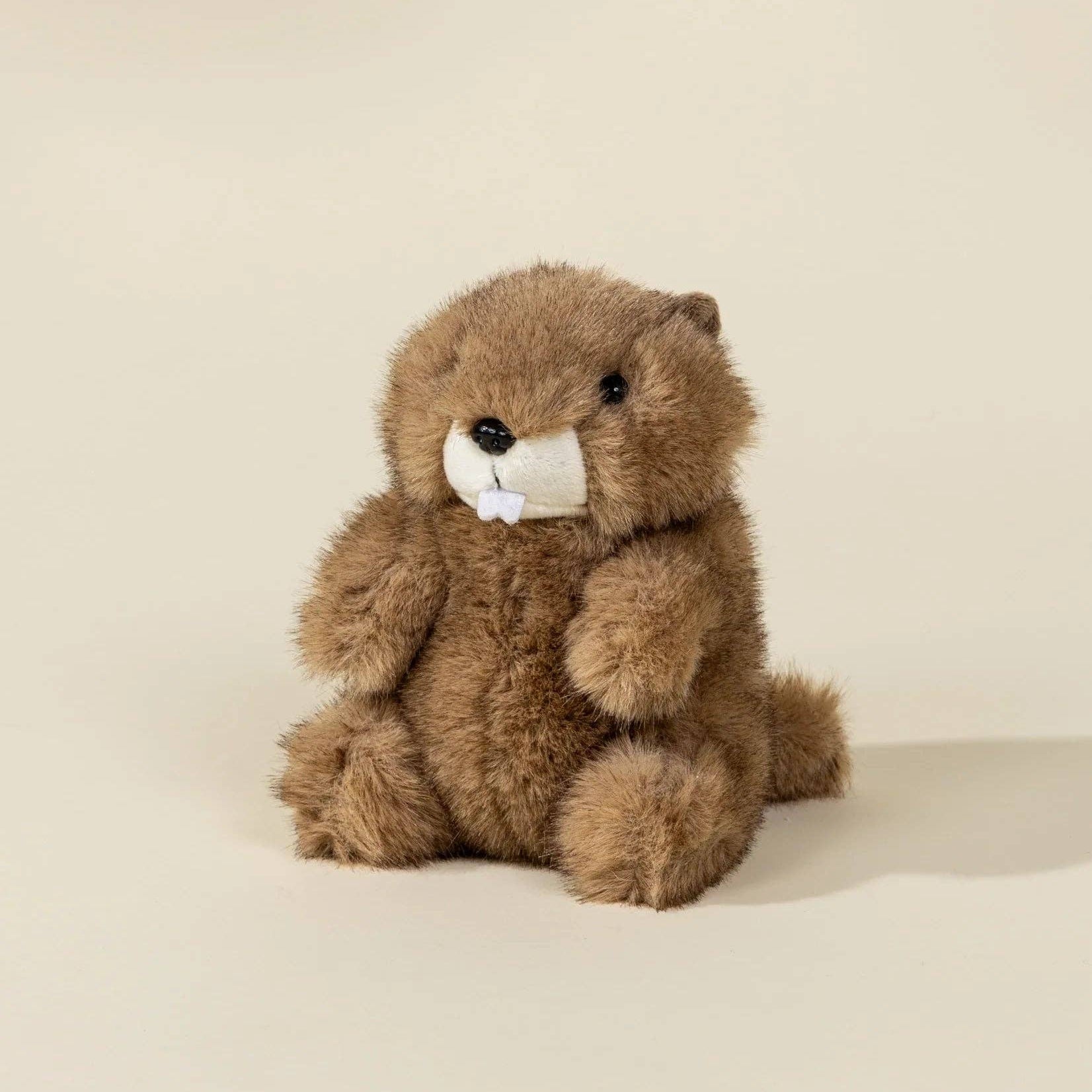 Brown plush toy sitting on a beige surface with a plain background