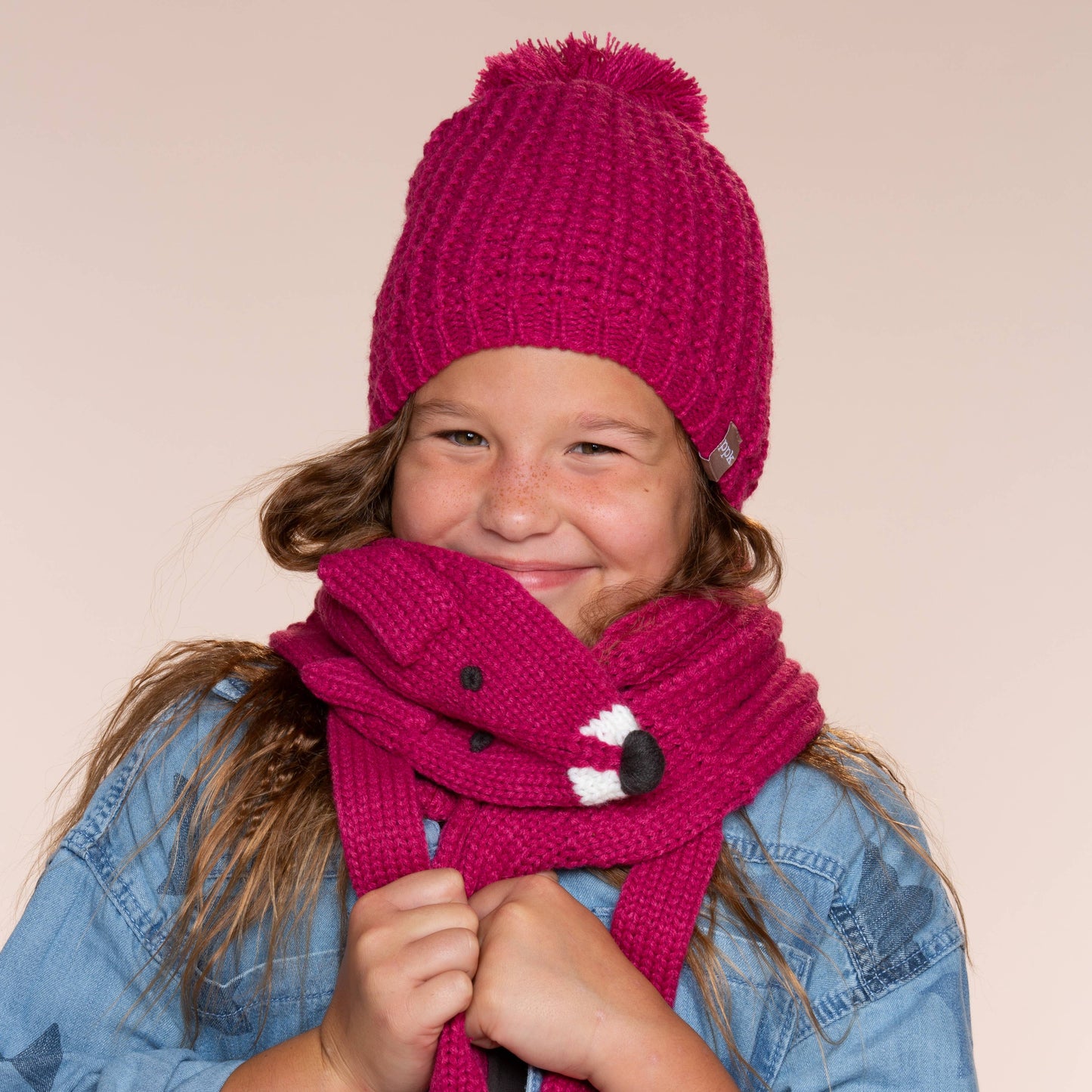 Child wearing a pink knit hat and scarf against a beige background