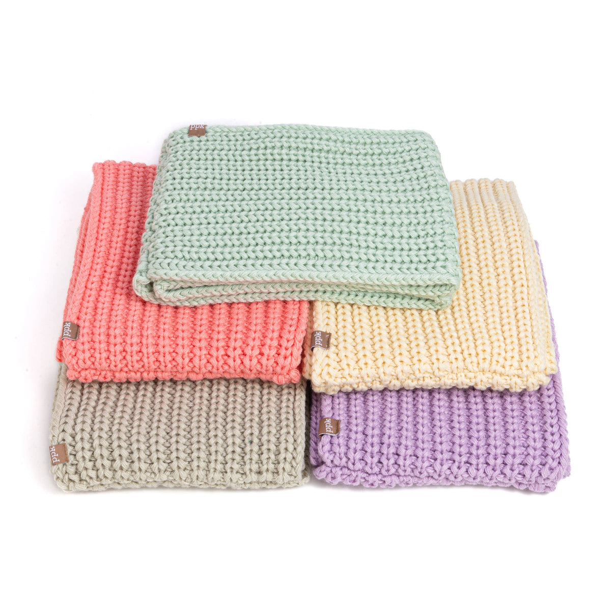 Four folded chunky knit scarves in pastel shades of sage green, coral pink, cream yellow, and lavender purple, stacked on a white background.