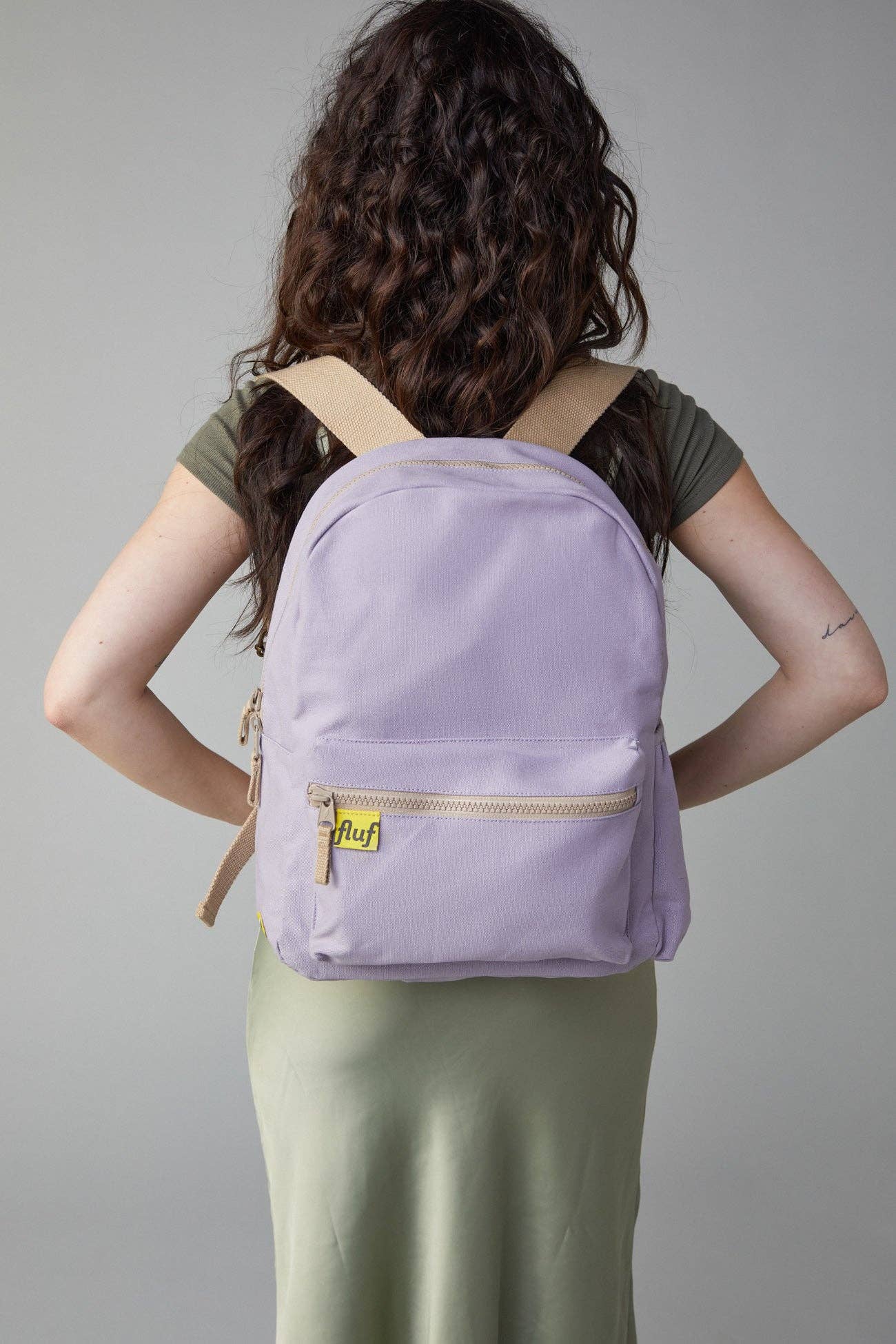 Person wearing a purple backpack with a gold zipper on a plain background
