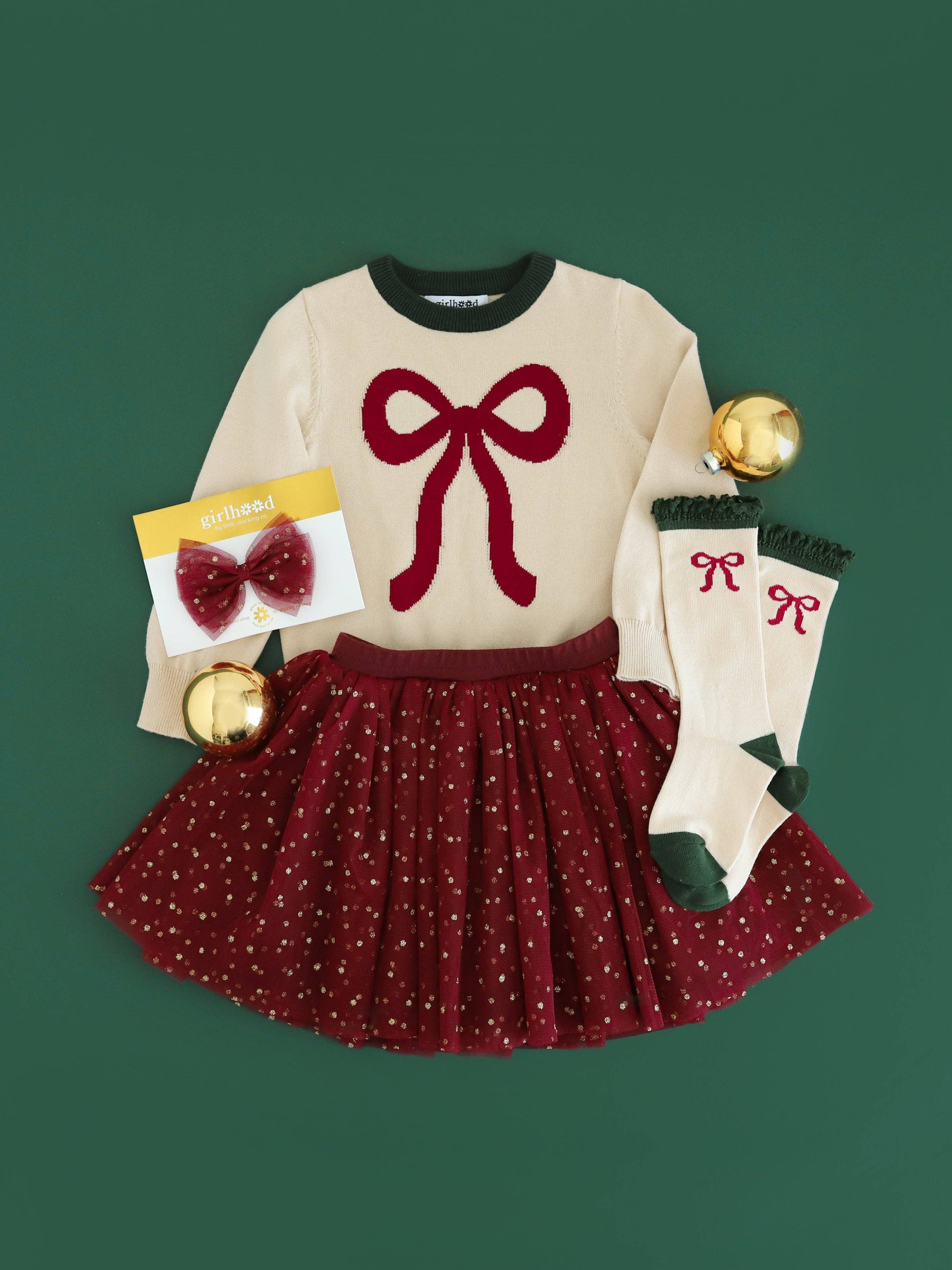 Children's outfit with sweater, skirt, socks, and accessories on a green background