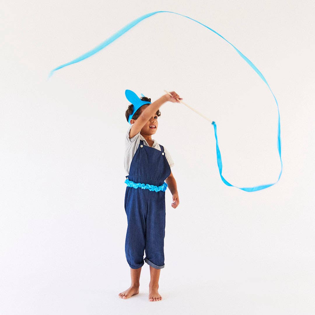 Child in blue overalls playing with a blue ribbon on a white background