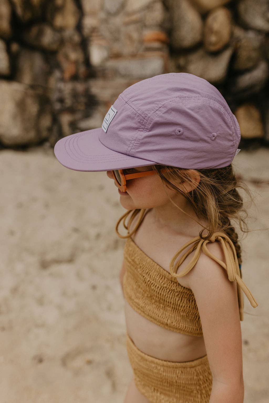 Child wearing a purple cap and yellow top against a stone wall background