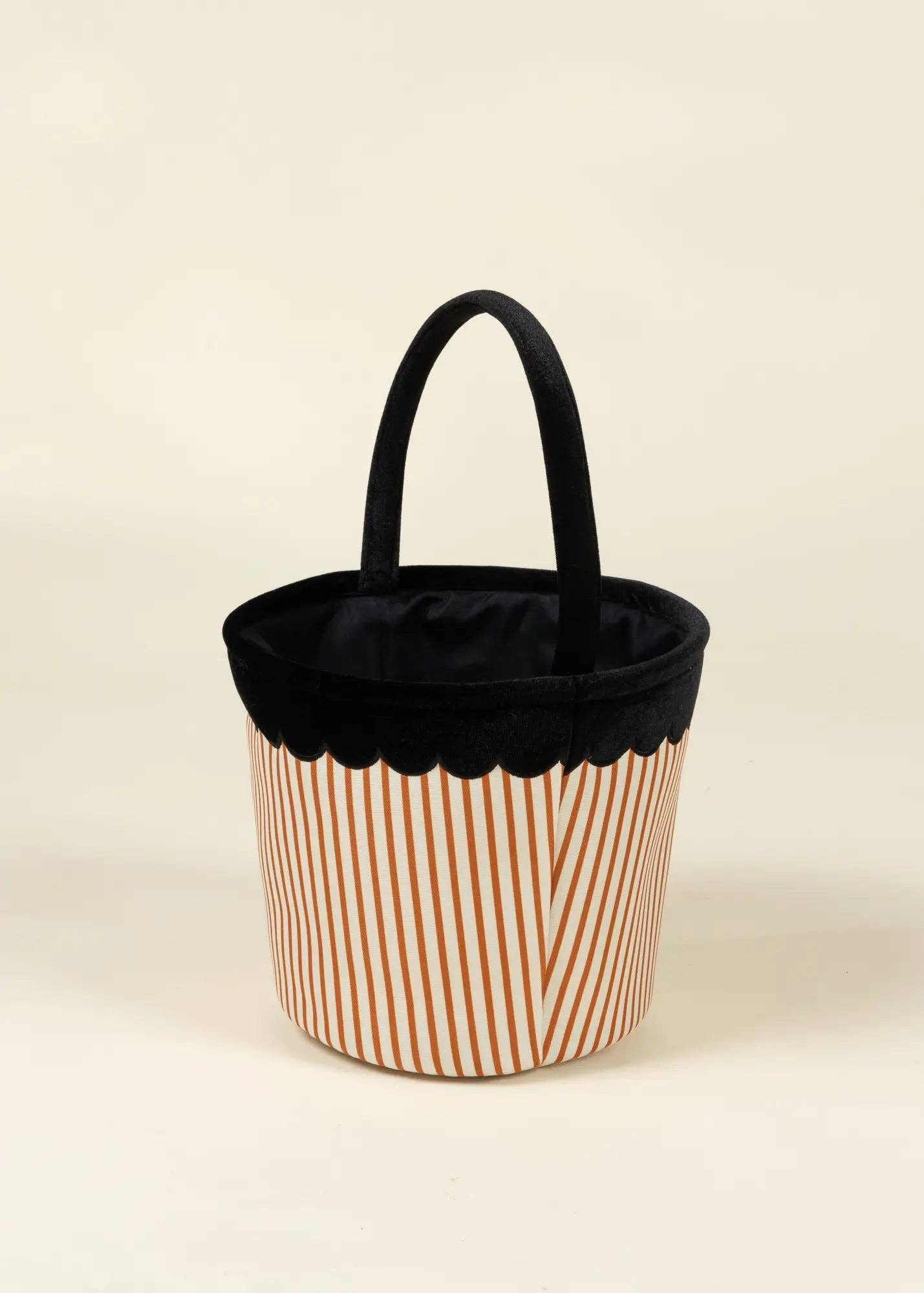 A cylindrical fabric tote bag with a black top handle, a black scalloped inner rim, and a body featuring thin vertical orange stripes on a white background.