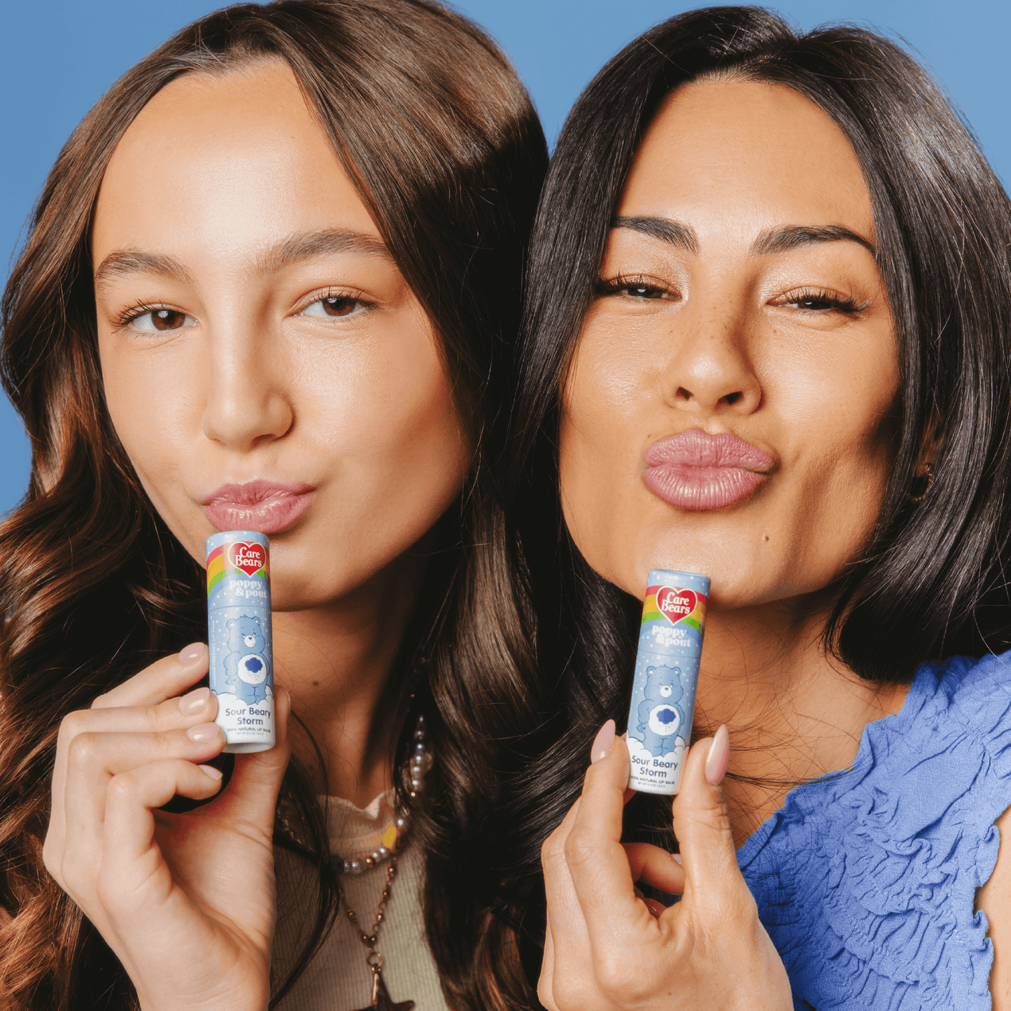 Two women holding and showing a lip balm against a blue background