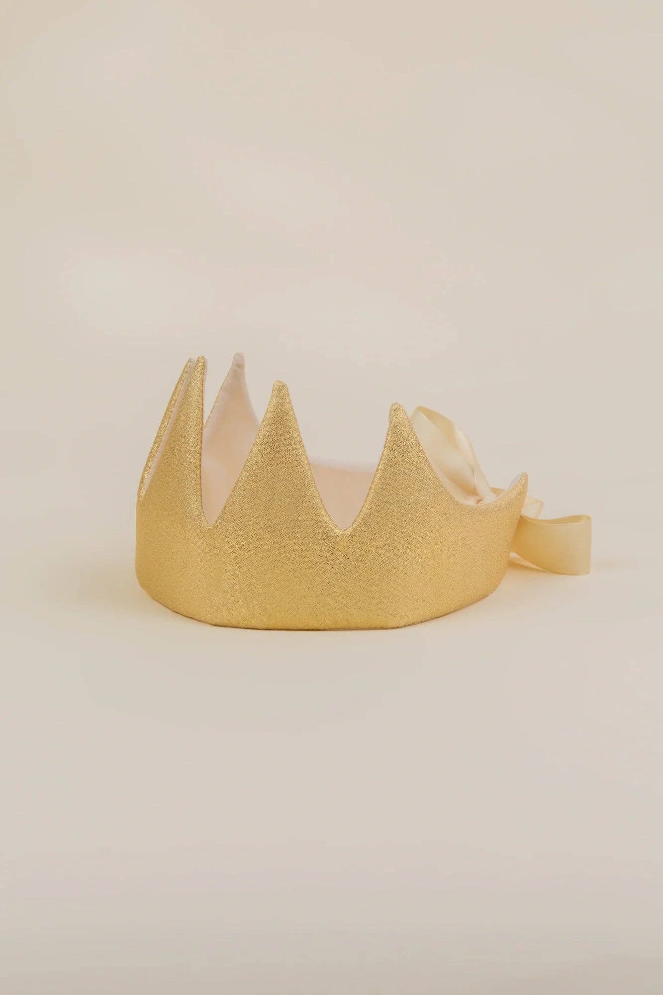 A gold glitter crown headband with a matching ribbon bow, displayed on a neutral cream background.