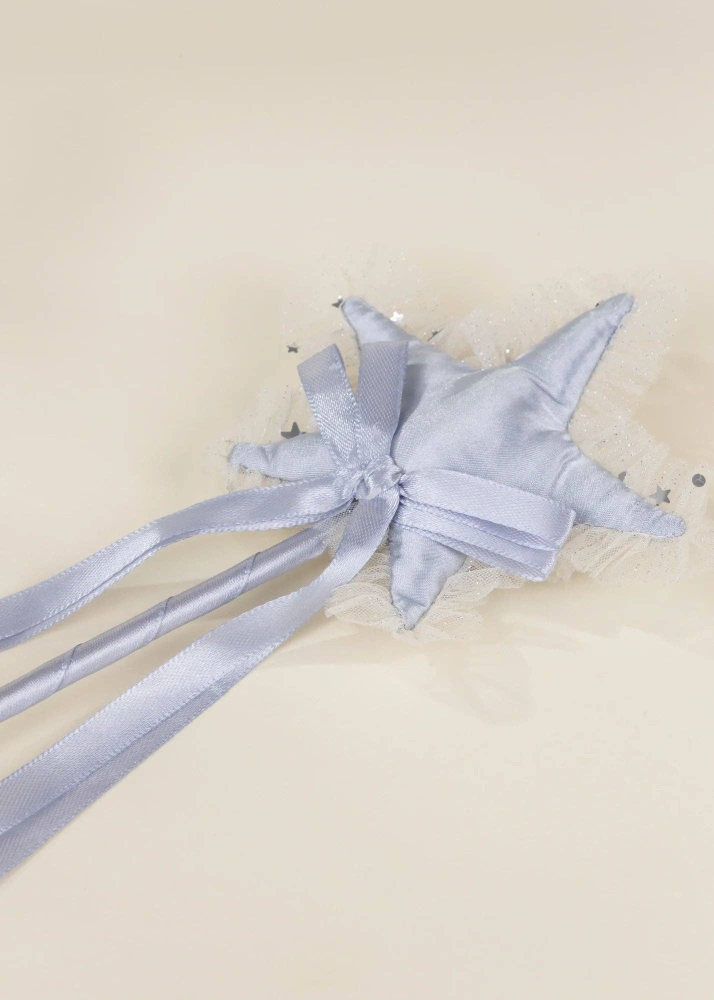 A light blue satin star-shaped hair accessory with a bow, tulle trim, and long ribbon tails, photographed on a plain cream background.