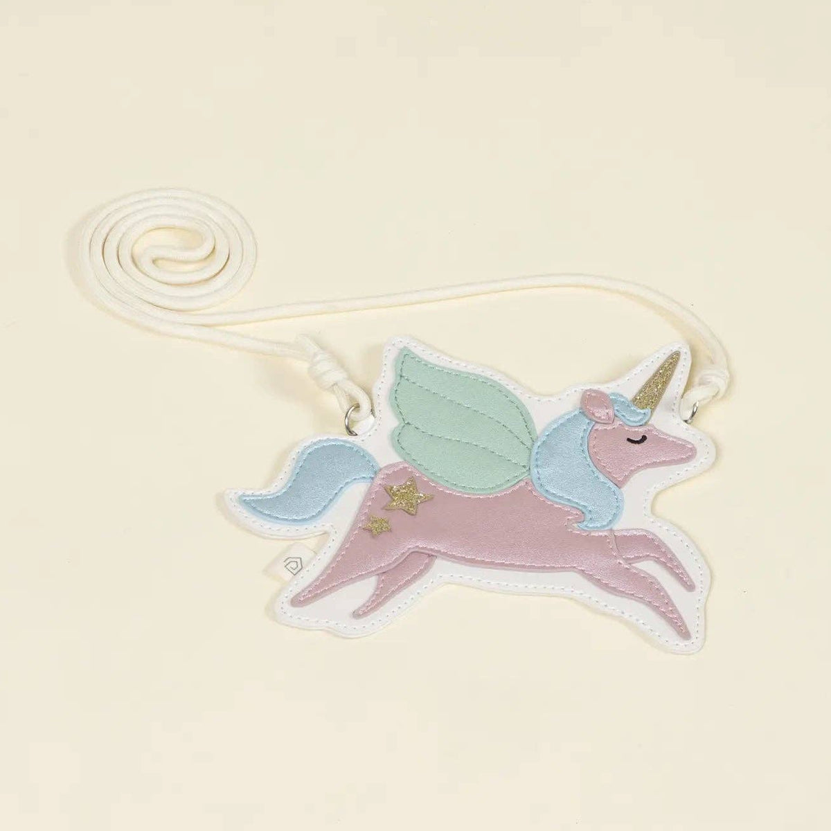 A pastel embroidered unicorn bag with wings, a horn, and a white looped ribbon, shown on a plain warm cream background.