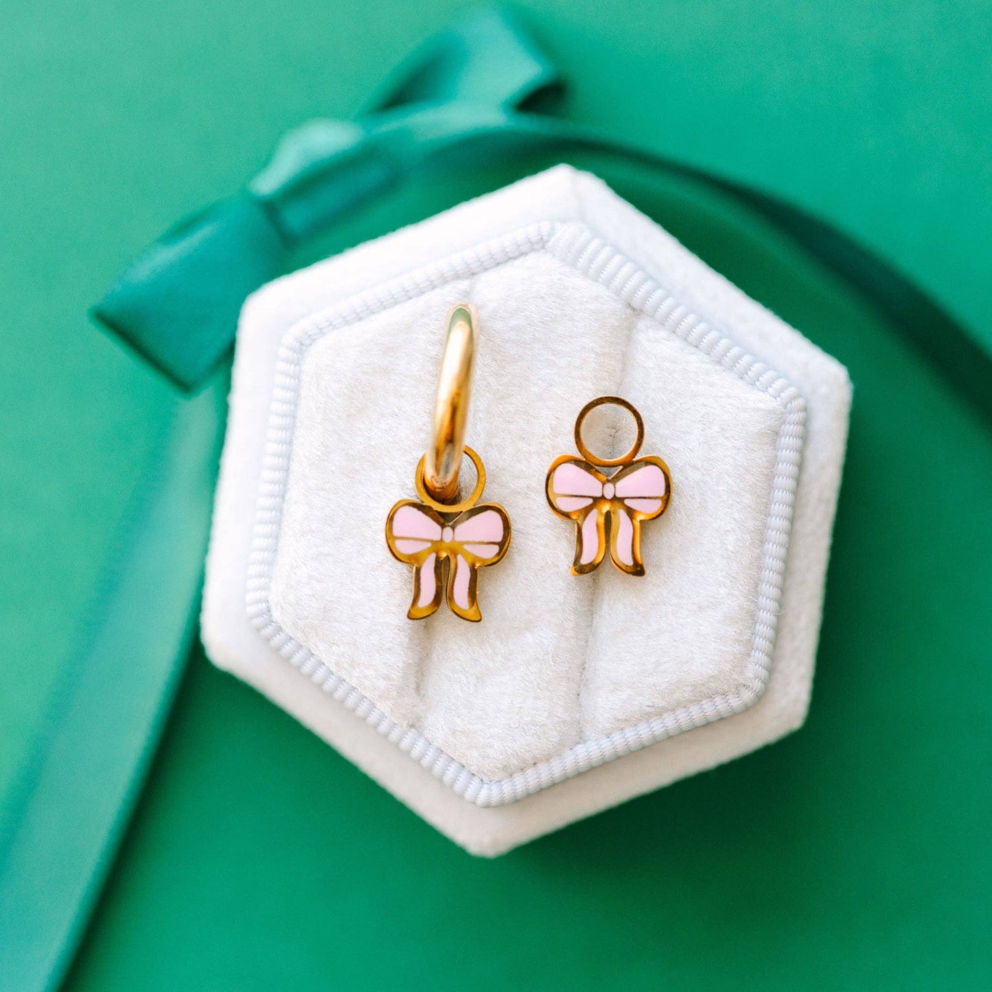 Earrings with pink bows in a hexagonal white case on a green background