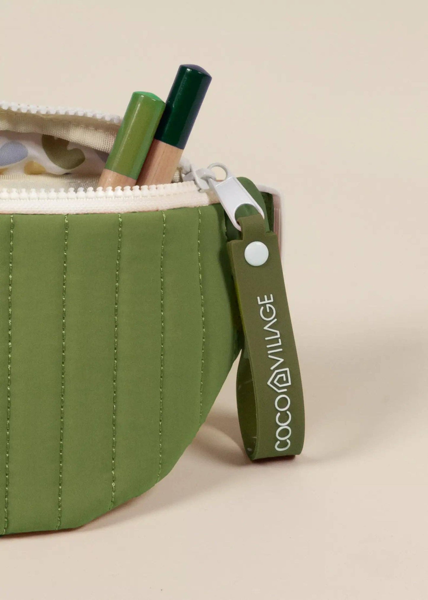 Green waist bag with a white zipper on a beige background