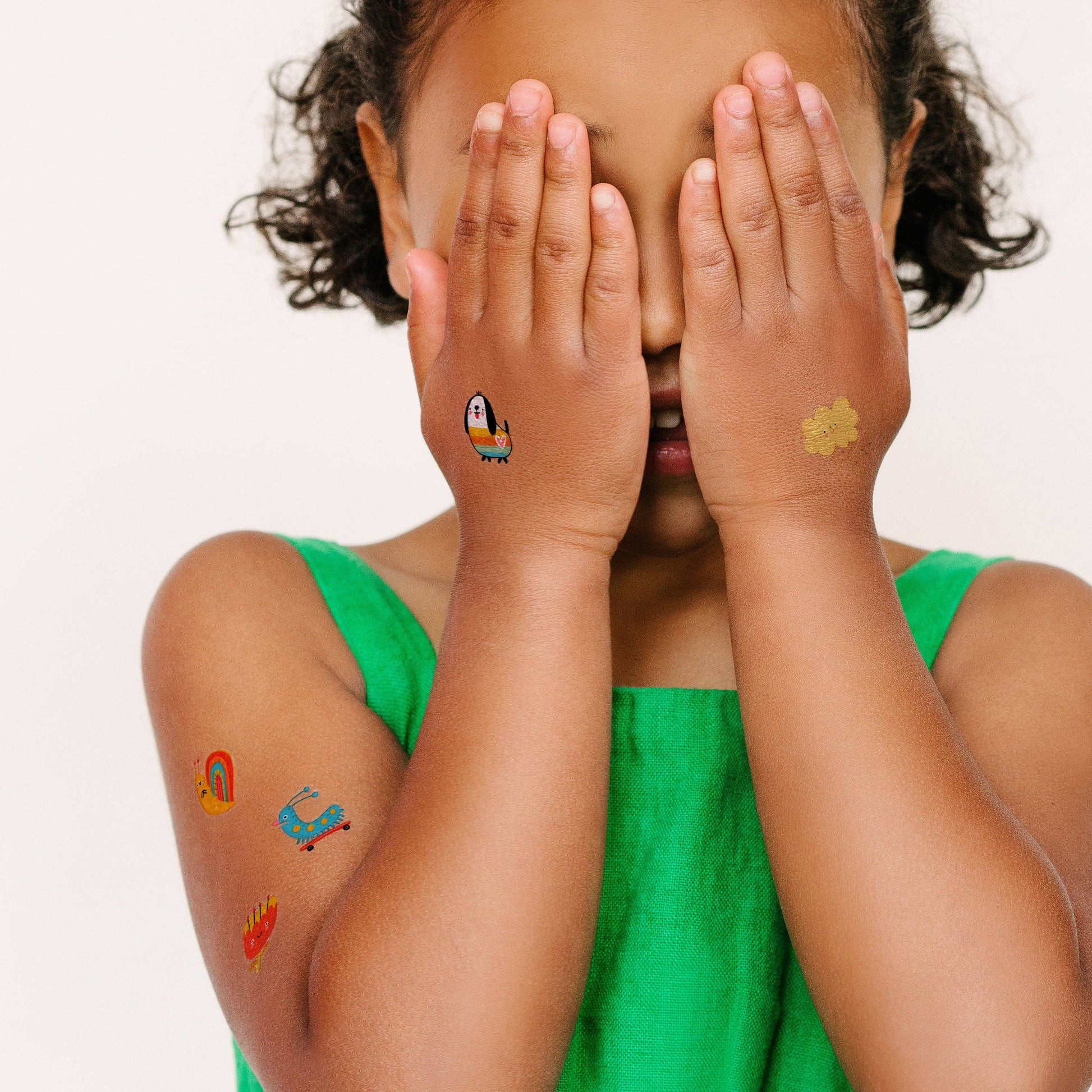 Child with temporary tattoos on arms and hands, wearing a green top.