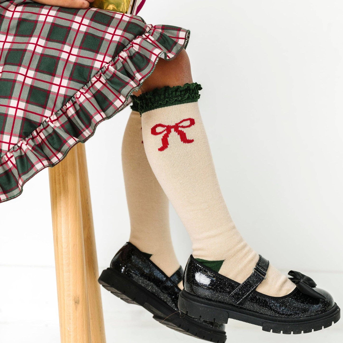 Person wearing knee-high socks with a red bow design, black shoes, and a plaid skirt.