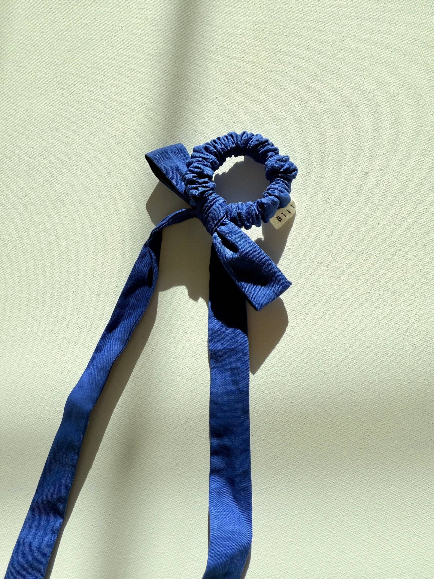 Blue scrunchie with a long ribbon on a beige background