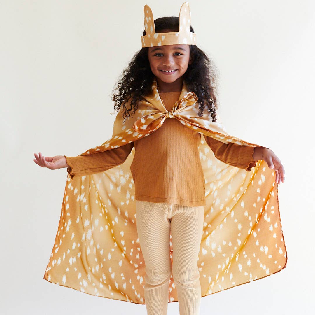 Child wearing a deer costume with a cape and headband on a white background