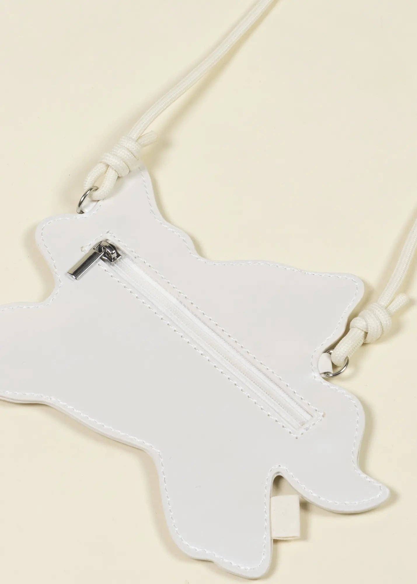 White faux leather crossbody bag with a unicorn-shaped silhouette, featuring a central zipper and white rope strap details, shown on a light cream background.