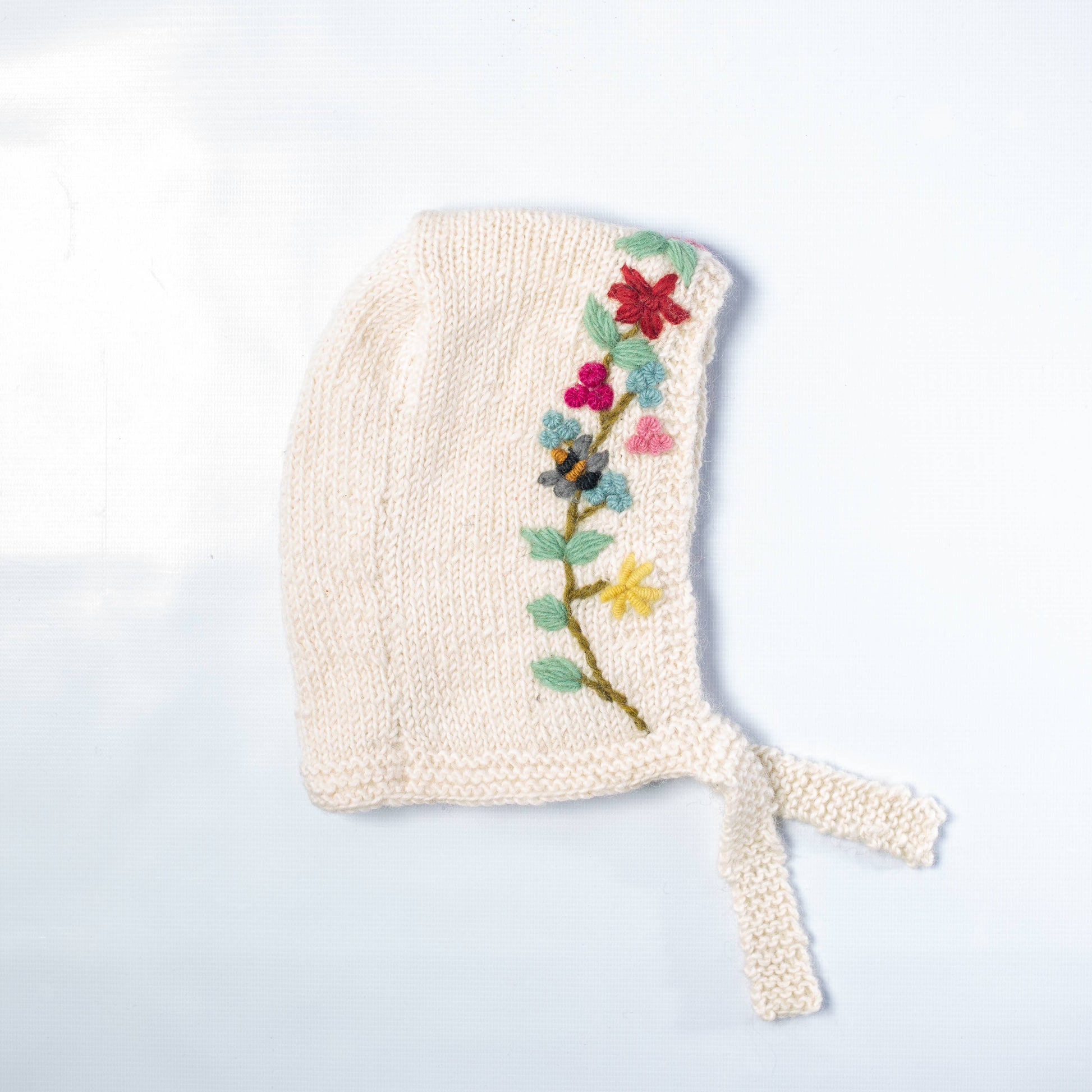 Knitted baby bonnet with floral embroidery on a light background