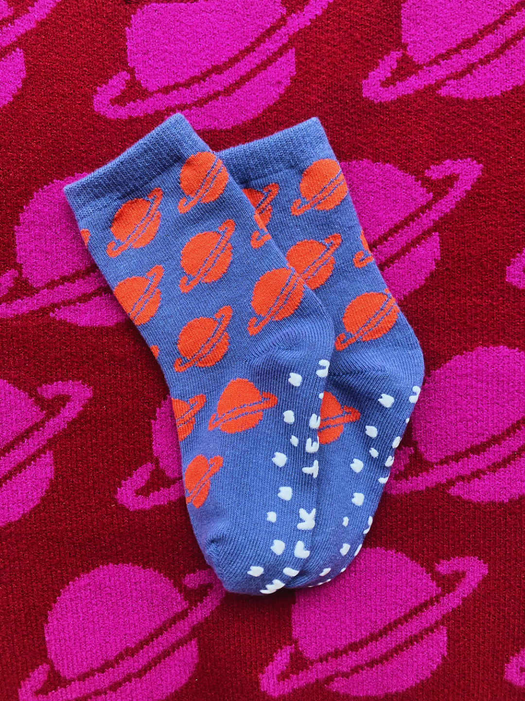 Blue socks with orange planet patterns on a red background with pink Saturn shapes.