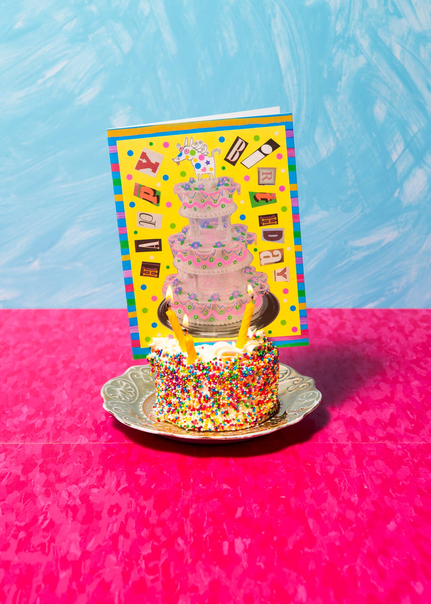 Colorful cake with sprinkles on a pink surface and blue background