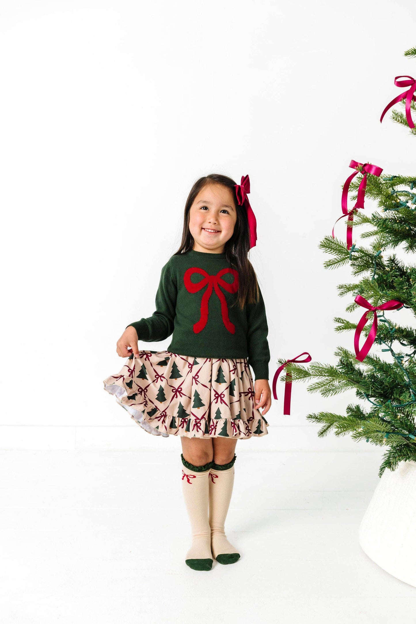 Young girl in festive outfit with Christmas tree and decorations on a white background